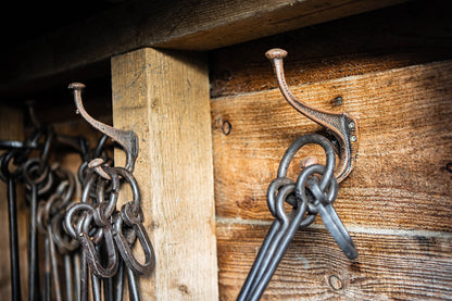 Rustic cast iron wall hooks mounted on wooden boards, used to hang traditional black metal fire tools and pokers.
