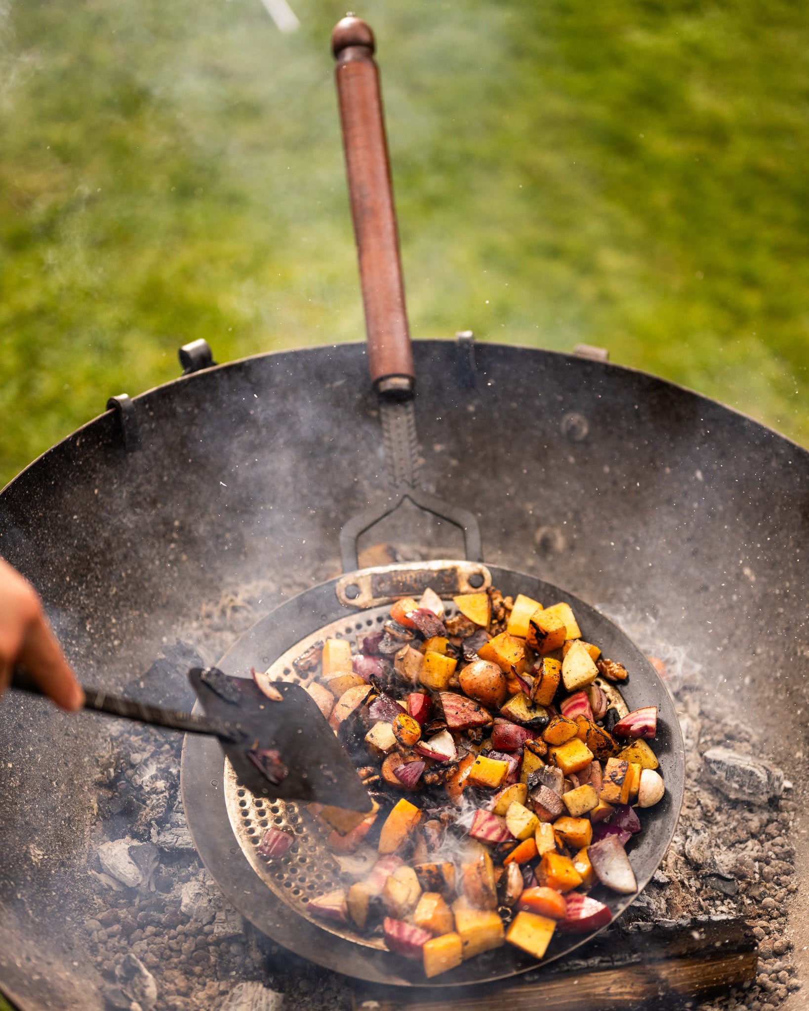 Zhara roasting pan with charred vegetables cooking over hot coals in a Kadai firebowl barbecue outdoors
