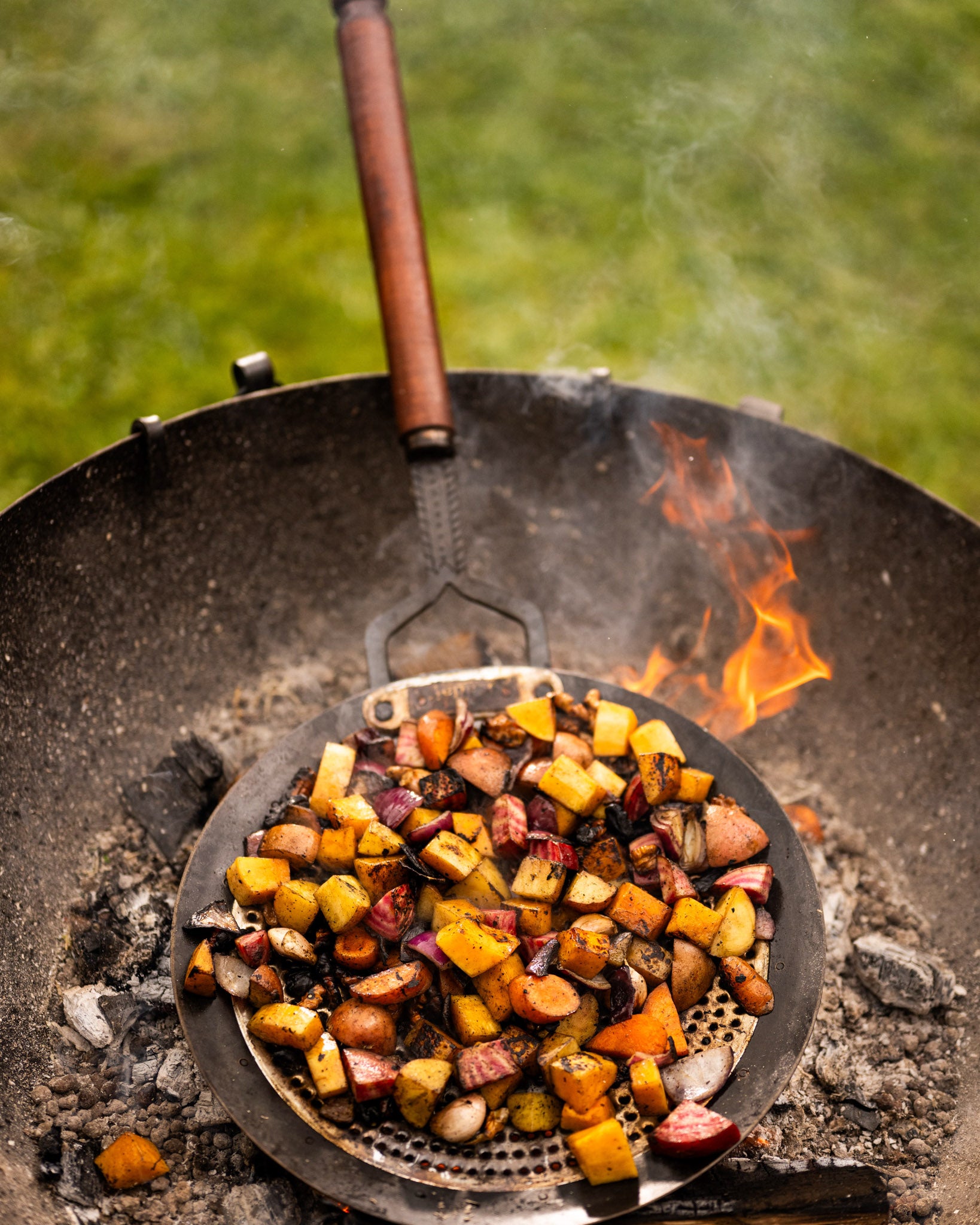 Zhara roasting pan with roasted vegetables cooking over open flames in a Kadai firebowl barbecue outdoors