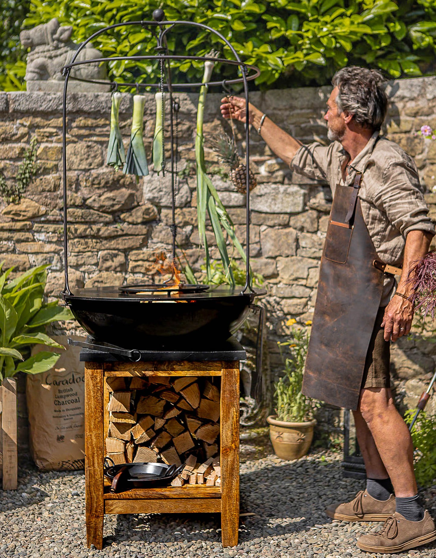 Man cooking on a plancha kadai grill with vegetables hanging above the fire
