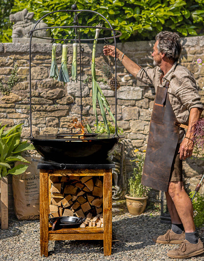 Man cooking on a plancha kadai grill with vegetables hanging above the fire