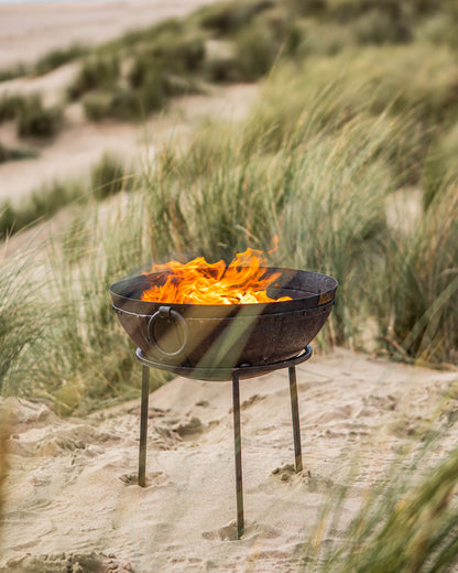 Small barbecue grill with flames on a sandy beach with grasses in the background
