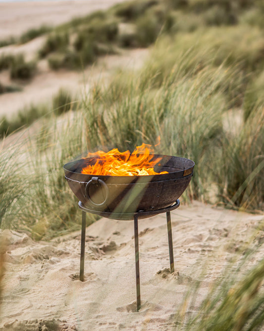 Small barbecue grill with flames on a sandy beach with grasses in the background