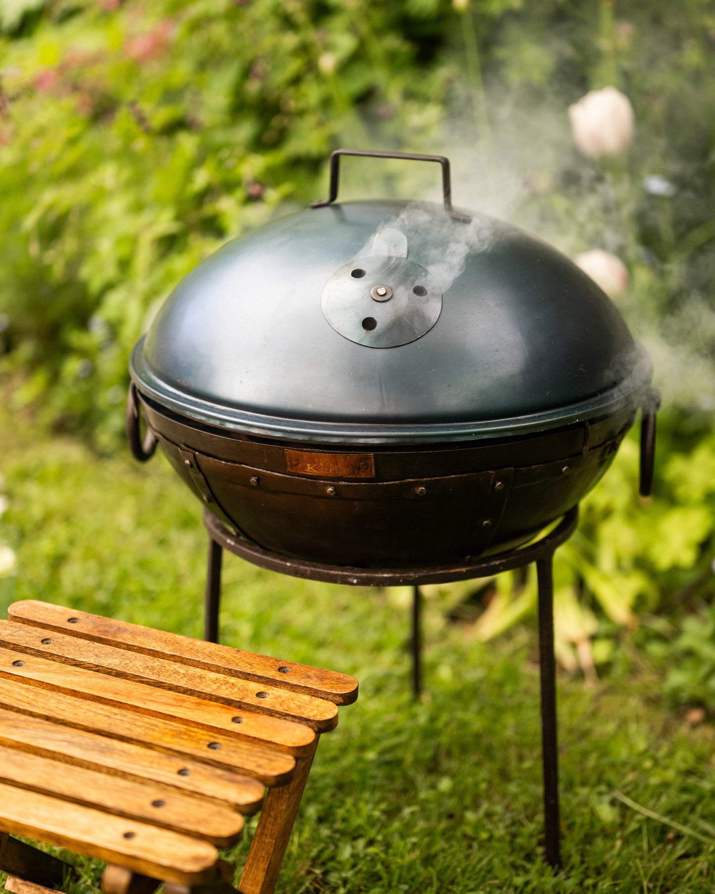 Black barbecue grill with smoke rising in a garden setting