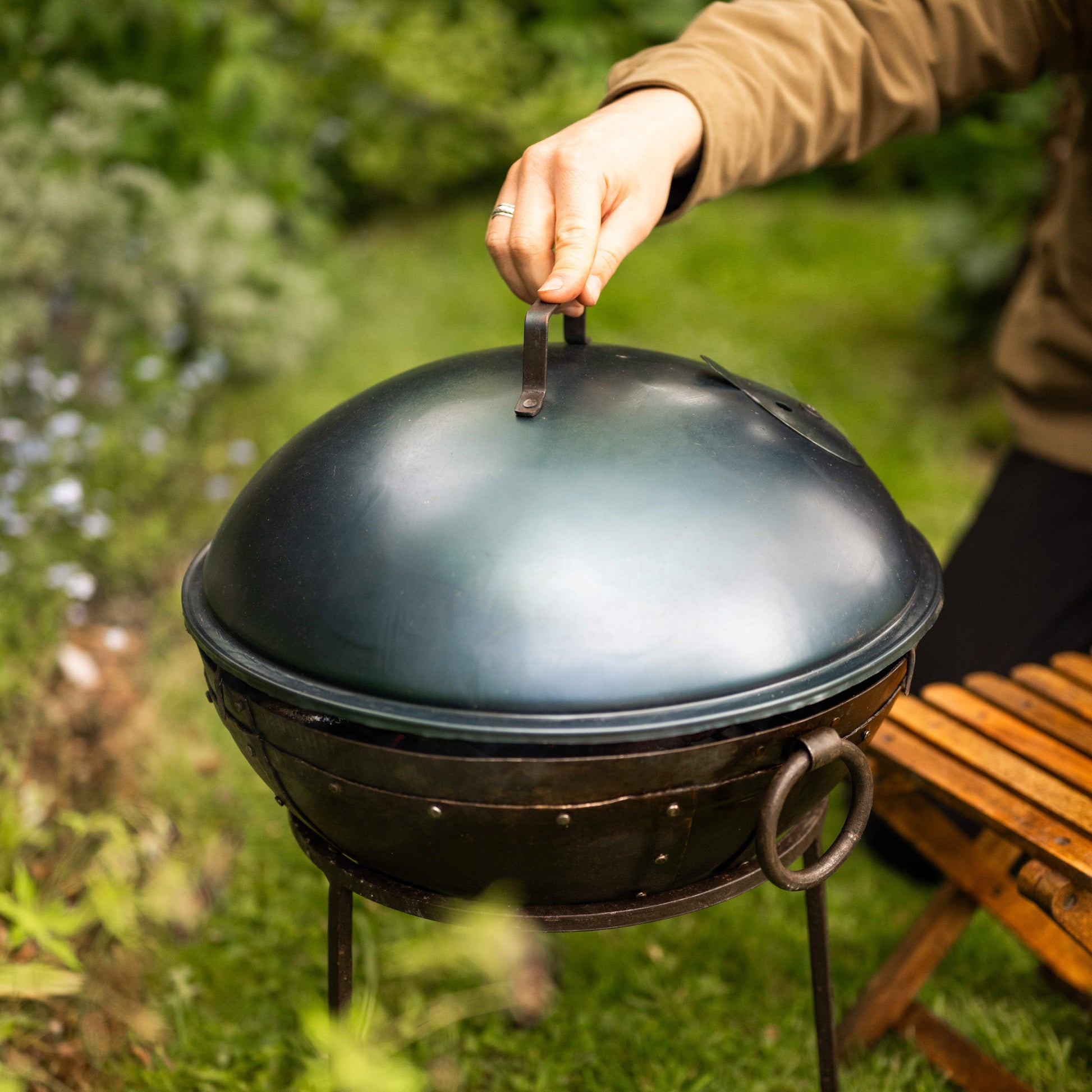 Portable BBQ lid with built-in air vent and carry handle on a traditional metal grill