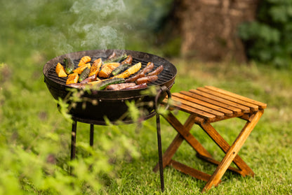 Portable BBQ in a garden with a stool, grilling vegetables 