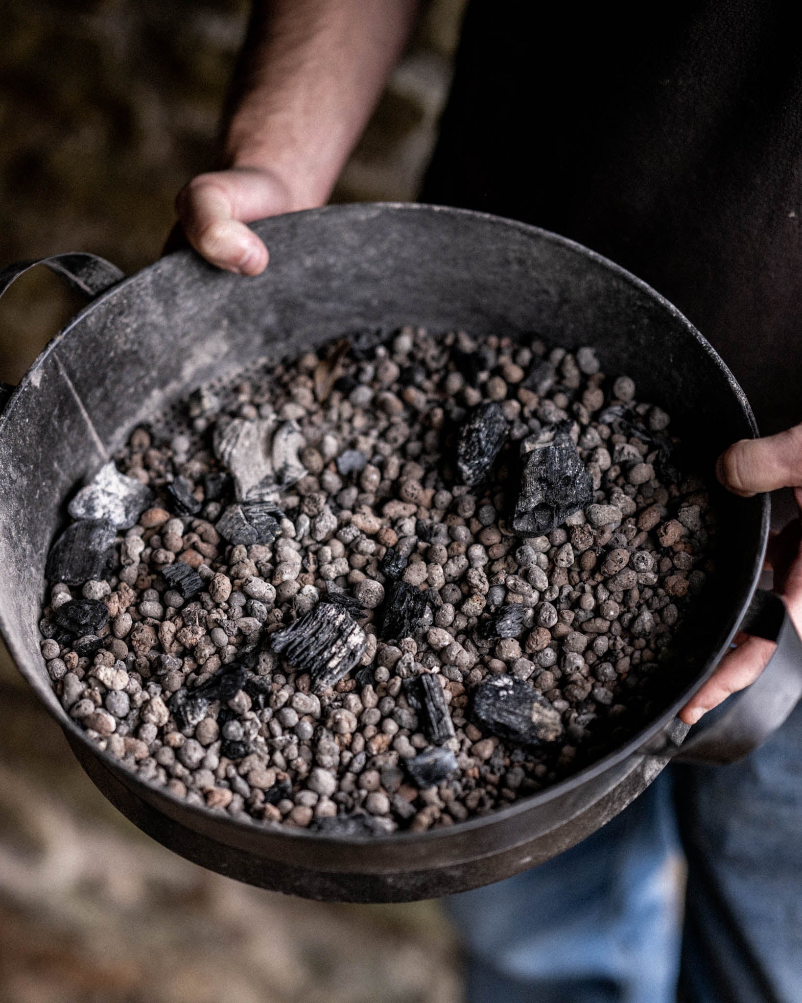 Close-up of a Kadai Riddle accessory containing ceramic beads and charcoal, designed for controlled outdoor cooking heat distribution