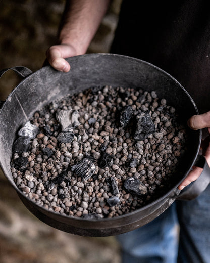 Close-up of a Kadai Riddle accessory containing ceramic beads and charcoal, designed for controlled outdoor cooking heat distribution