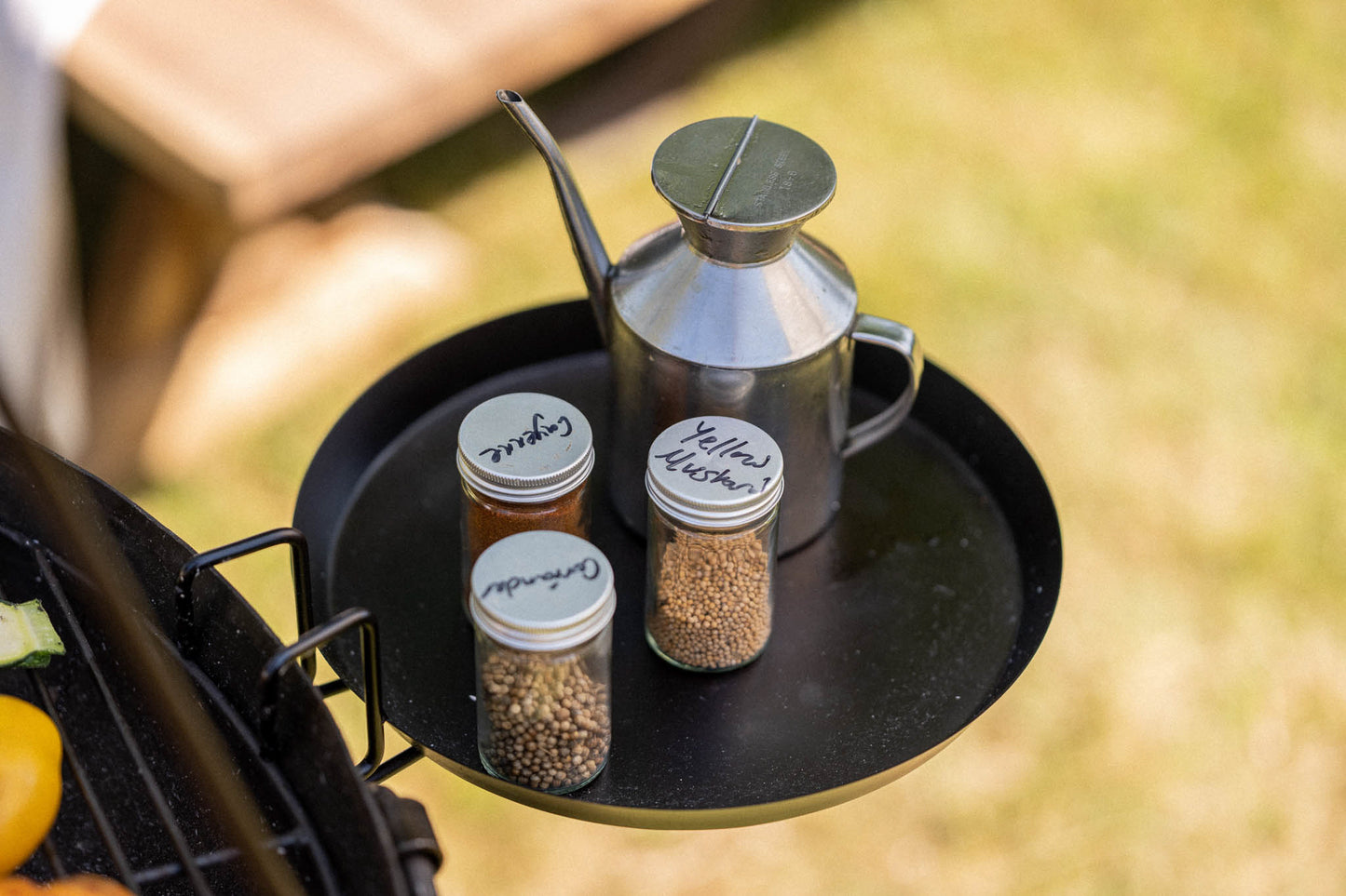 Minimalist black Kadai side shelf accessory holding spice jars and a metal oil can for convenient outdoor cooking preparation