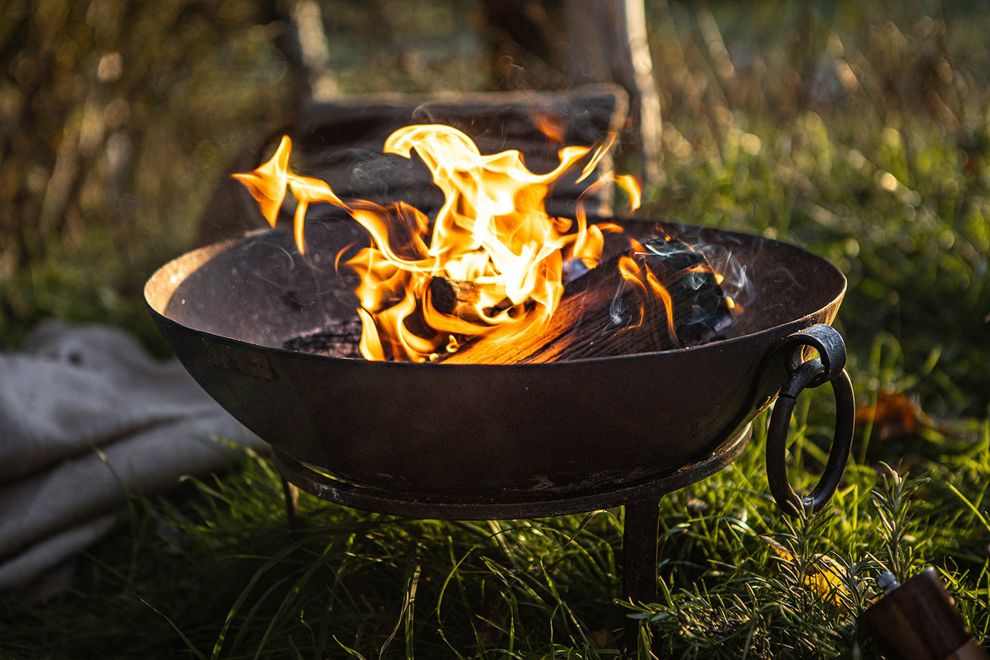 Garden fire pit with burning logs in a Kadai firebowl, flames rising in a grassy outdoor setting