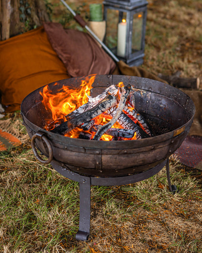 Medium sized charcoal BBQ fire bowl with burning logs and glowing embers in outdoor garden setting
