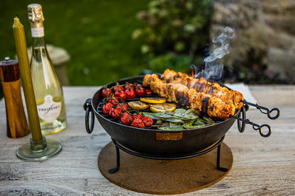 Outdoor BBQ table with Kadai fire bowl cooking skewers, tomatoes and greens over live fire