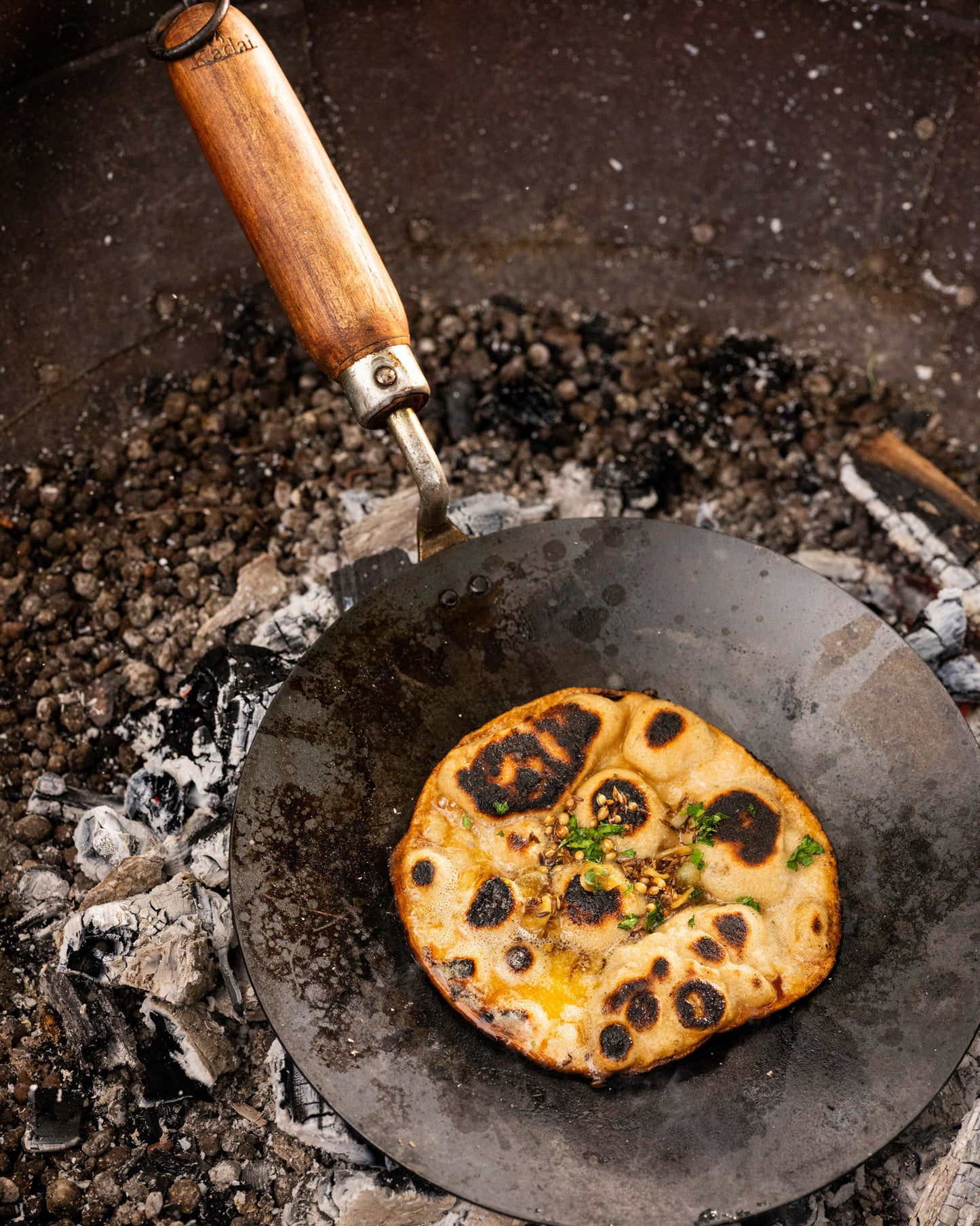 Flatbread being cooked on a hot stone surface with a kadai chapati pan.