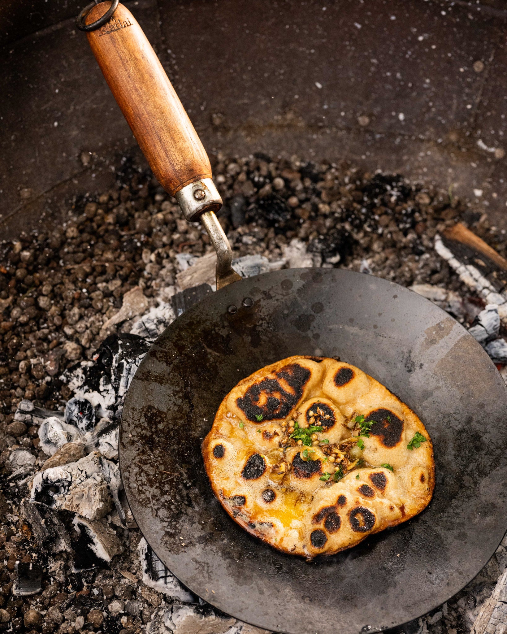 Flatbread being cooked on a hot stone surface with a kadai chapati pan.