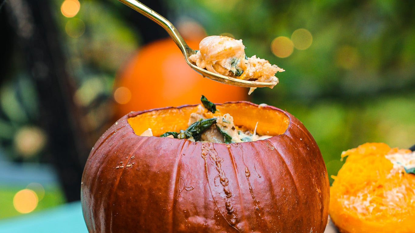 Person spooning out food from a pumpkin with a festive blurred out background.