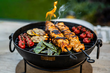 Outdoor BBQ table with Kadai fire bowl cooking skewers, tomatoes and greens with flames rising