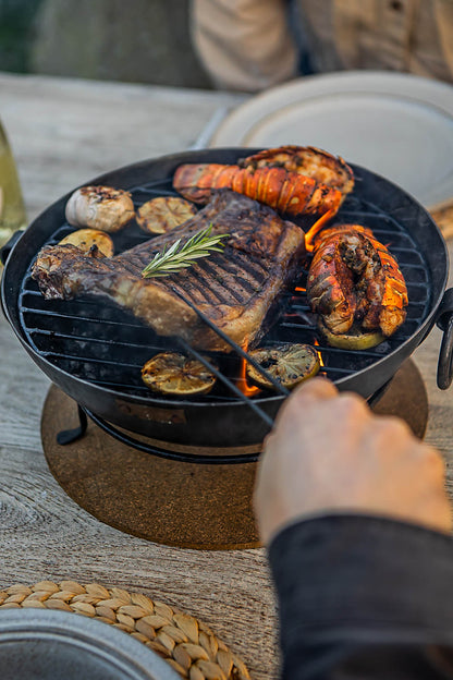 Outdoor BBQ table with Kadai fire bowl cooking steak and seafood on grill with flames underneath
