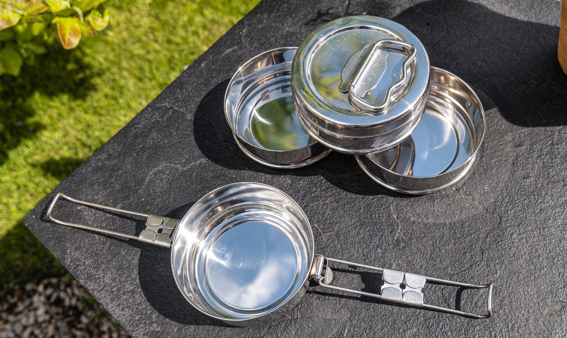 Set of metal tiffin tin containers on a stone surface with greenery in the background