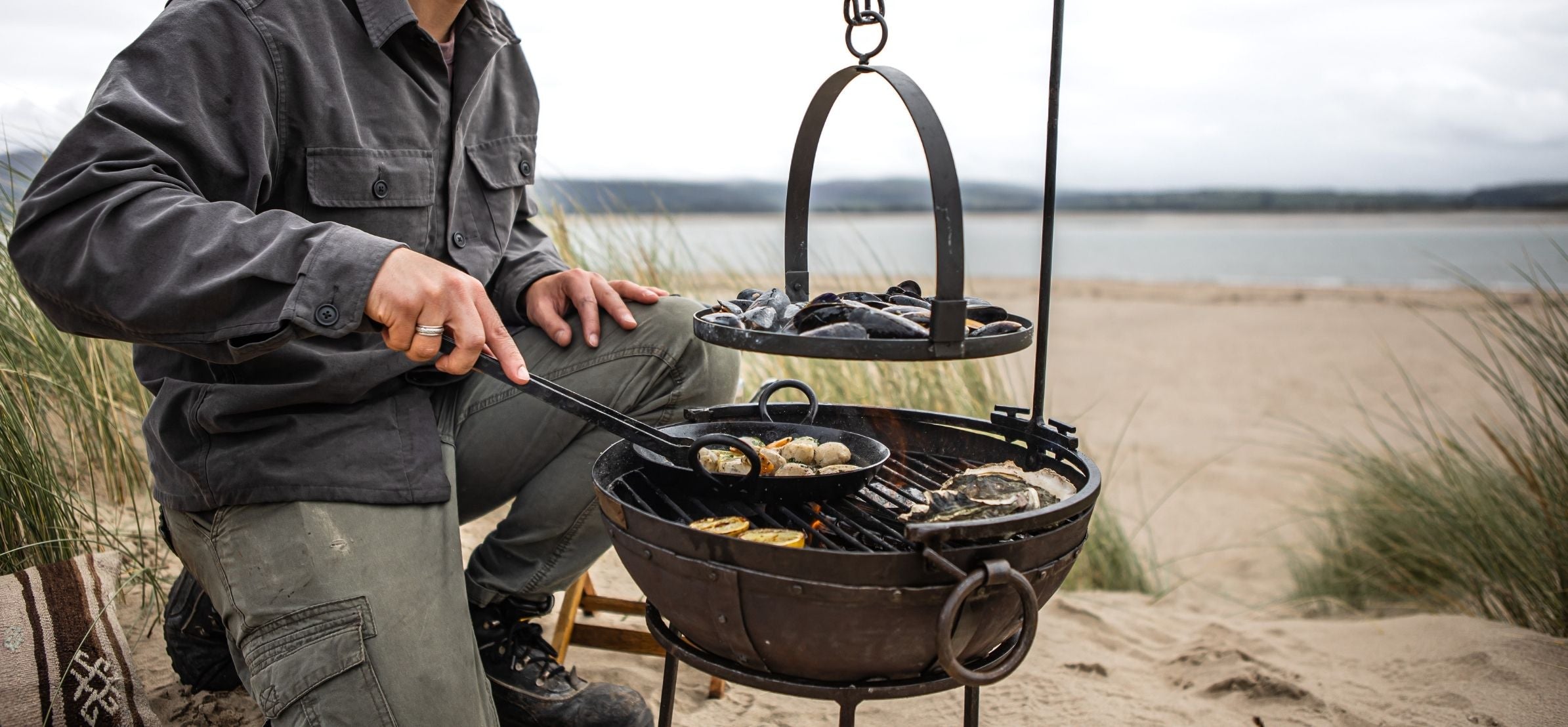 Person cooking outdoors using a portable grill by the beach