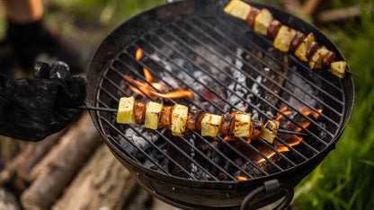 Skewer of pineapple and sausage cooking over open flames on a portable BBQ skillet grill