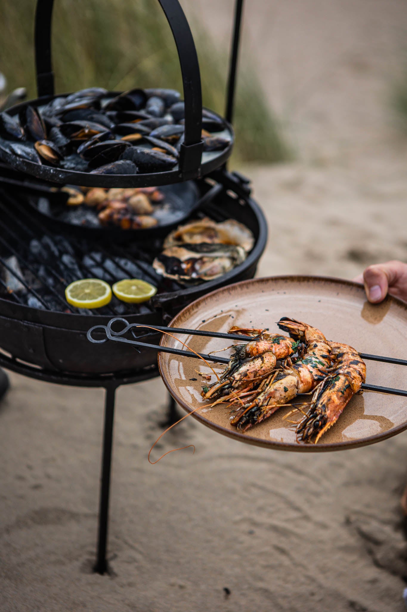 Grilled prawns served on a plate beside a portable BBQ skillet cooking seafood over coals