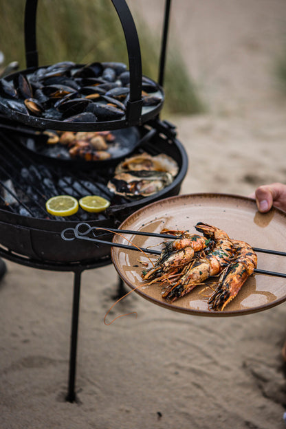 Grilled prawns served on a plate beside a portable BBQ skillet cooking seafood over coals