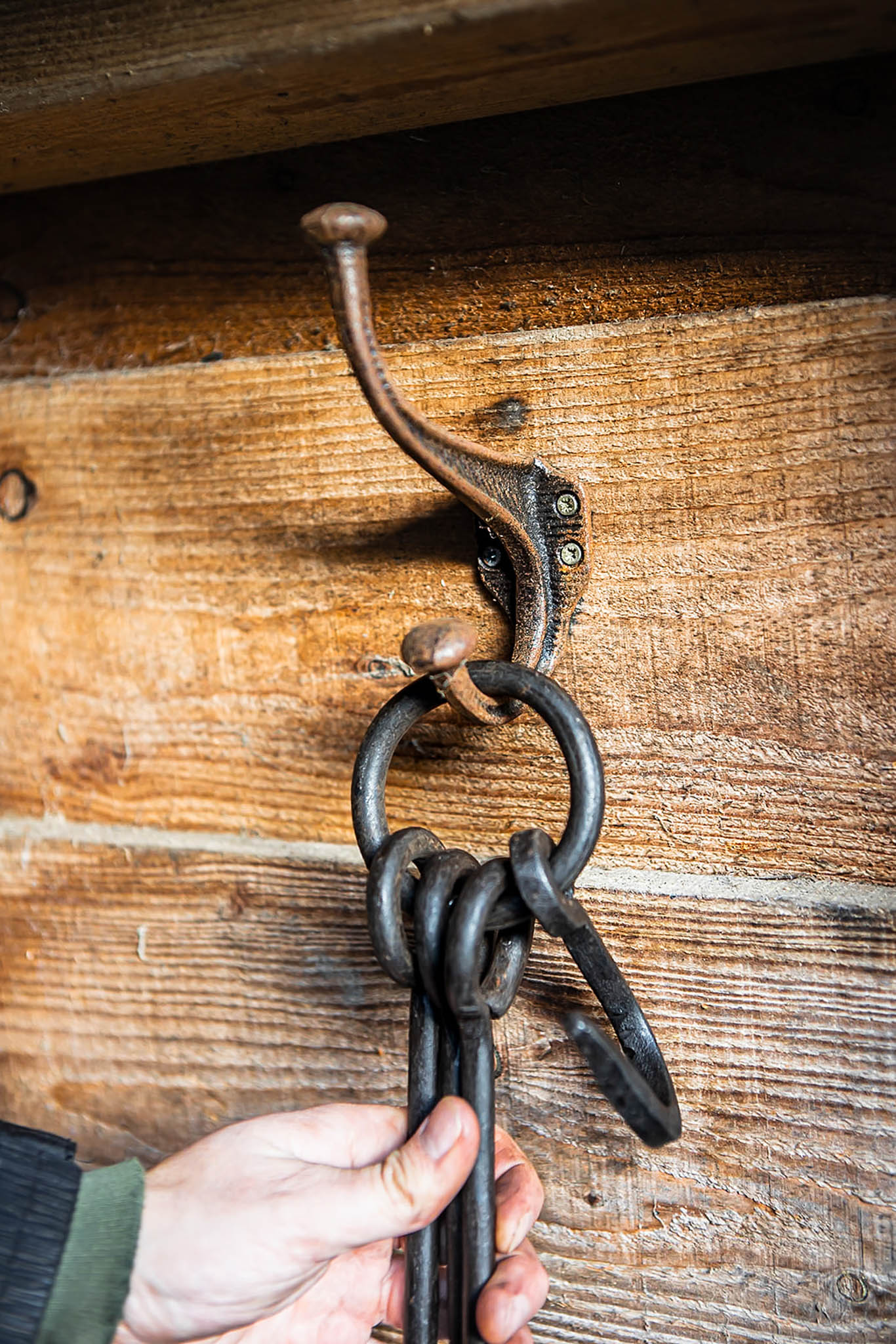 Rustic cast iron wall hook mounted on wooden boards, holding black metal fire tools on a hanging ring.