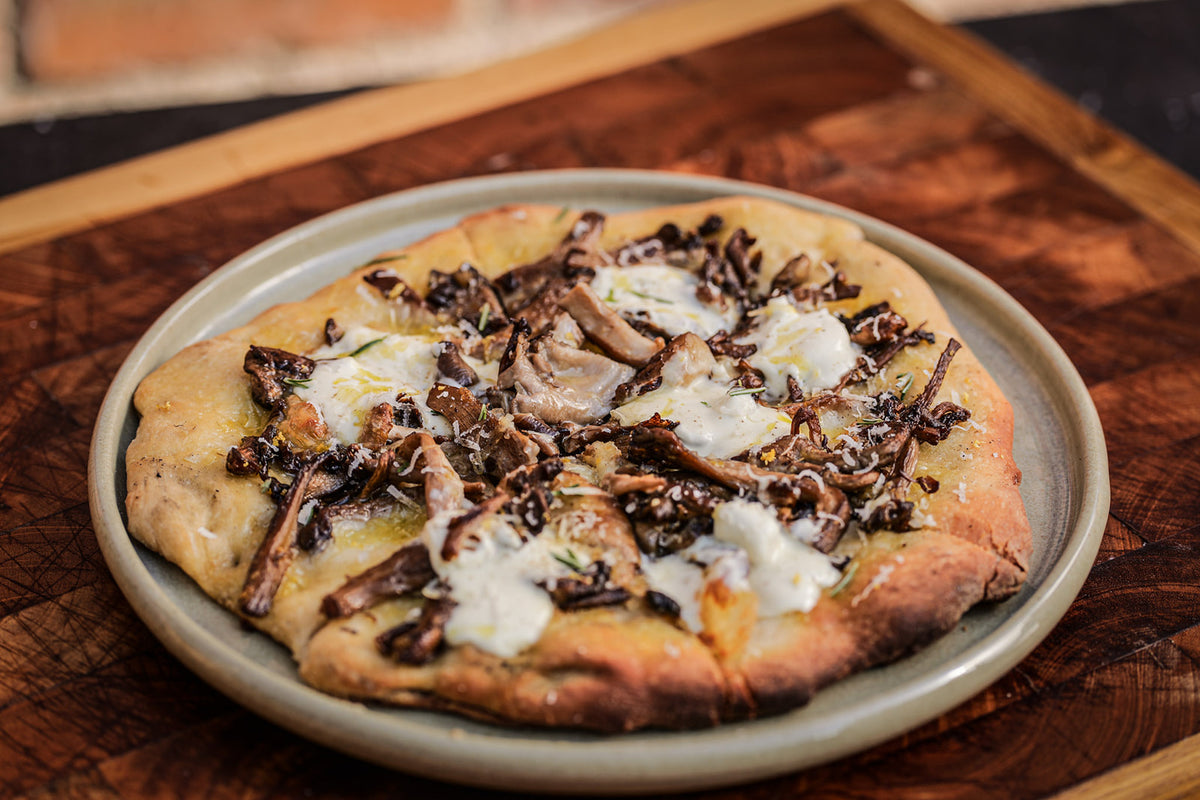 a round pizza on a plate on a wooden chopping board. The pizza is topped with cheese, mushrooms, parmesan and lemon zest.