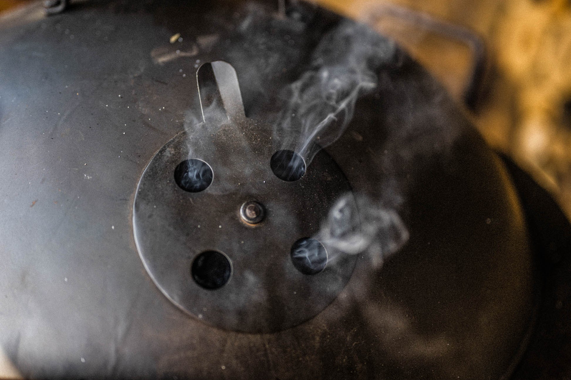 Top of a smoker box lid with smoke coming out of the vents.
