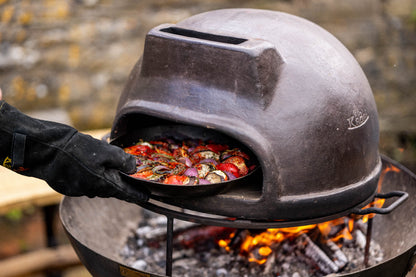 Close-up of an outdoor oven dish with vegetables being cooked inside a covered grill over hot coals