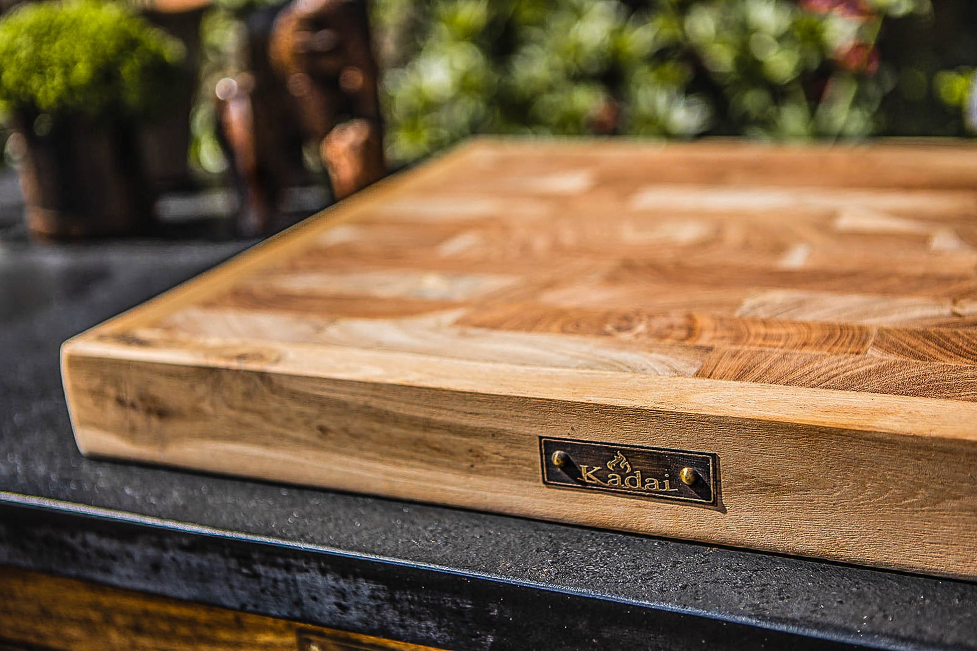 Close-up of a thick wooden butcher’s block with visible end-grain pattern and Kadai branding on an outdoor kitchen counter.